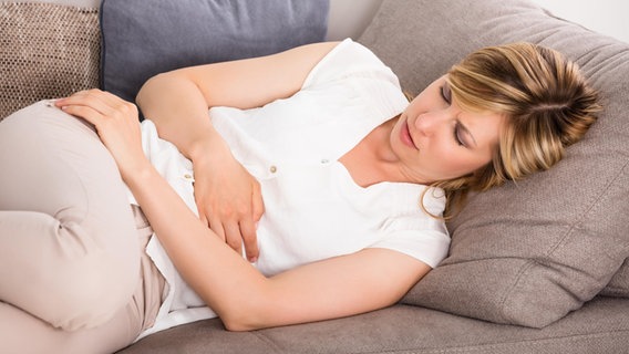 Eine junge Frau liegt auf dem Sofa und hält sich die Hände vor den Bauch. © picture alliance / PantherMedia | Andriy Popov Foto: Andriy Popov