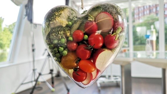 Ein Glasherz gefüllt mit Tomaten, Erbsen etc. hängt in der Luft. © NDR Foto: Katja Gundlach