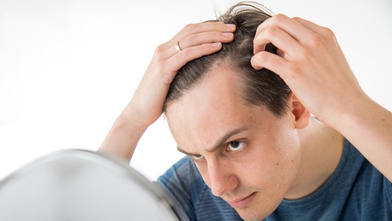 Ein junger Mann begutachtet seinen Haaransatz im Spiegel. © picture alliance/dpa Themendienst Foto: Christin Klose