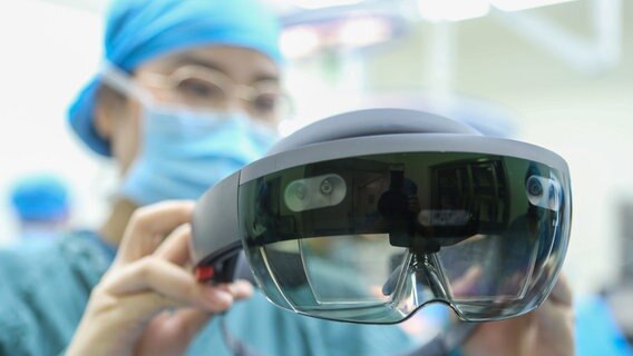 Eine Ärztin in OP-Kittel hält eine Augmented-Reality-Brille in der Hand. © picture alliance/dpa/HPIC | Lao Qiang 