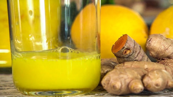 Ein selbstgemachter Ingwershot in einem Glas steht neben frischem Ingwer.  
