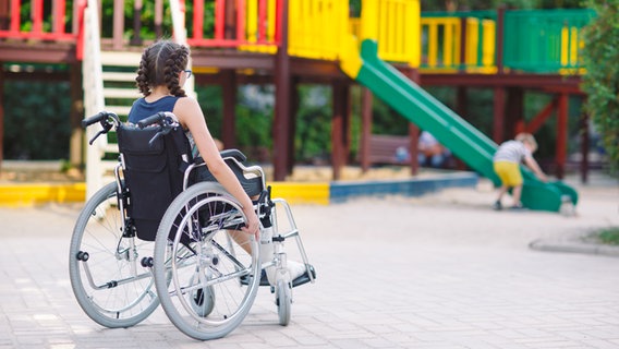Ein Mädchen sitzt in einem Rollstuhl und schaut auf dem Spielplatz einem anderen Kind beim Spielen zu. © Colourbox Foto: #282776