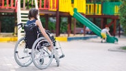 Ein Mädchen sitzt in einem Rollstuhl und schaut auf dem Spielplatz einem anderen Kind beim Spielen zu. © Colourbox Foto: #282776