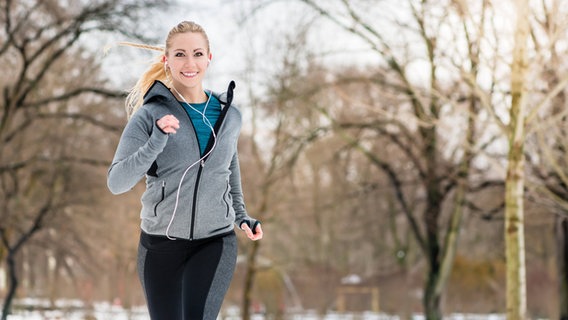 Eine junge Frau joggt durch eine Winterlandschaft. © IMAGO / YAY Images Foto: IMAGO / YAY Images