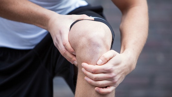 Ein Mann in Sportbekleidung fasst sich an sein Knie. © picture alliance/dpa Themendienst 