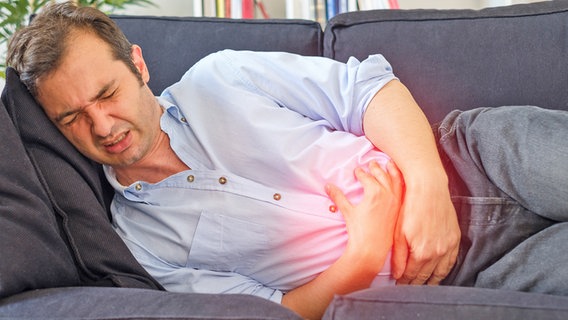 Ein Mann liegt mit Magenschmerzen auf dem Sofa. © imago images Foto: tommaso79