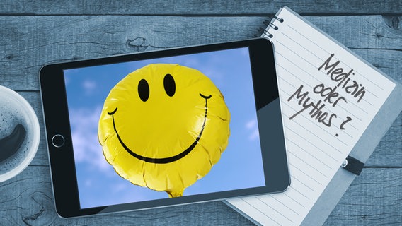 Auf einem Tisch liegt ein Tablet mit einem Bild von einem Smiley. Auf einem Notizblock sind die  Worte "Medizin oder Mythos" zu lesen (Montage) © Colourbox / Fotoalia Foto: Blackzheep/Stephen Coburn
