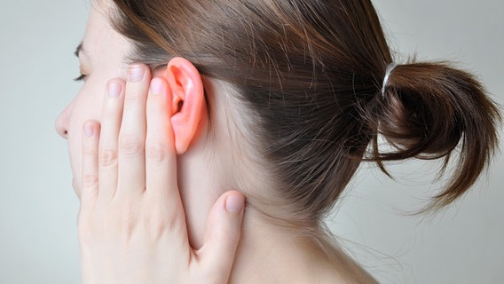 Frau mit schmerzverzerrtem Gesicht legt Hand an ihr Ohr © colourbox.de 
