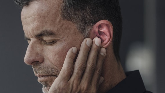 Mann mit schmerzverzerrtem Gesicht fasst sich an Ohr © IMAGO/Westend61 