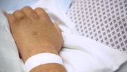 Bild zeigt in Nahaufnahme die Hand eines verstorbenen Patienten, die auf der Bettdecke liegt. © NDR 