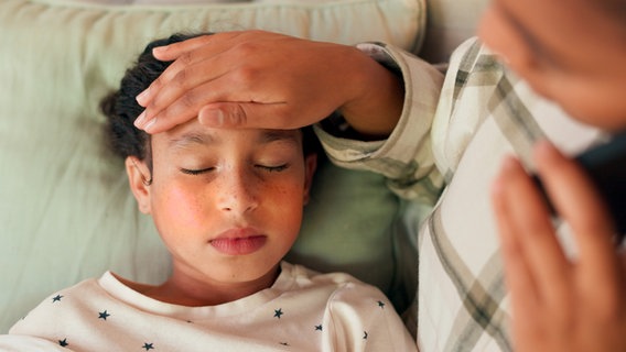 Krankes Kind liegt mit Fieber im Bett, die Hand der Mutter auf der Stirn © colourbox.de 