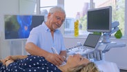 Dr. Jörn Klasen sitzt neben der Patientin Charline W., die auf einer Liege liegt, und untersucht ihre Schilddrüse. © NDR 