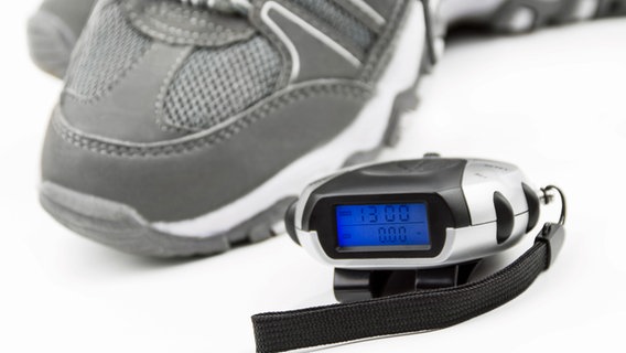 Ein Schritt- und Kalorienzähler liegt neben einem Turnschuh. © fotolia.com Foto: PhotoSG