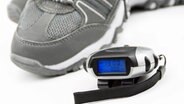 Ein Schritt- und Kalorienzähler liegt neben einem Turnschuh. © fotolia.com Foto: PhotoSG