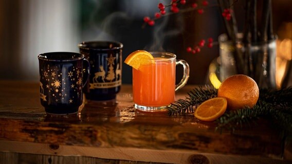 Zwei Tassen mit Glühwein und ein Orangen-Punsch stehen auf einem weihnachtlich geschmückten Tisch. © picture alliance / Zoonar | Marco Martins Foto: picture alliance / Zoonar | Marco Martins