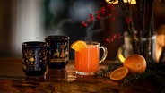 Zwei Tassen mit Glühwein und ein Orangen-Punsch stehen auf einem weihnachtlich geschmückten Tisch. © picture alliance / Zoonar | Marco Martins Foto: picture alliance / Zoonar | Marco Martins