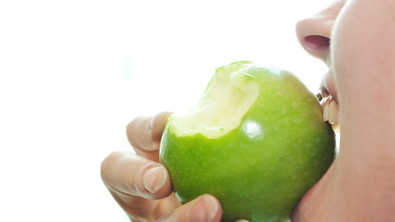 Eine Frau beißt in einen Apfel. © picture alliance / dpa Themendienst 