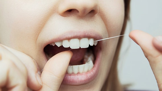 Frau fädelt Zahnseide zwischen ihre Zähne © Fotolia.com Foto: Two Brains Studio