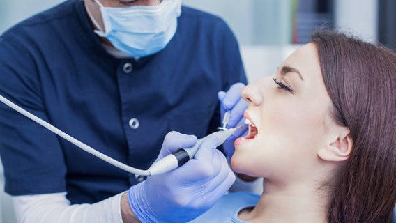 Ein Zahnarzt reinigt die Zähne einer Frau. © PantherMedia Foto: PantherMedia / Nikodash