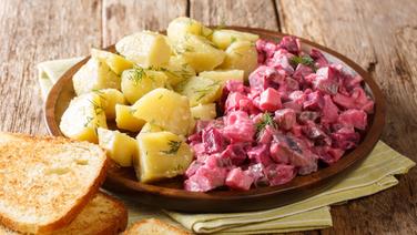Roter Heringssalat mit Kartoffeln auf einem Teller angerichtet, daneben liegen Weißbrotscheiben. © colourbox Foto: Sergii