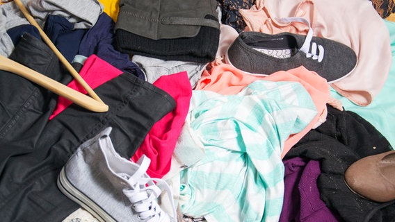 Verschiedene Kleidungsstücke, Schuhe und ein Kleiderbügel liegen auf einem Haufen. © Colourbox Foto: -