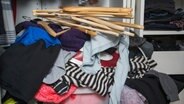 Verschiedene Kleidungsstücke und Kleiderbügel liegen vor einem Schrank. © Colourbox Foto: -