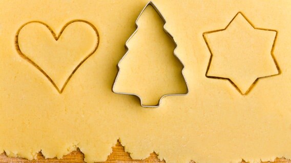 Ausgerollter Teig mit einem Ausstecher in Tannenbaum-Form und zwei bereits ausgestochenen Teigstücken in Stern- und Herzform. © Fotolia/Robert Kneschke 