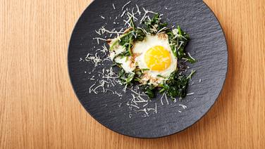 A fried egg on a bed of spinach served on a rustic dark plate.  © Joshua Stolz / solisTV 