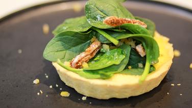Gorgonzola tart with spinach salad and salted lemons served on a black plate.  © Thomas Mudersbach / solisTV 