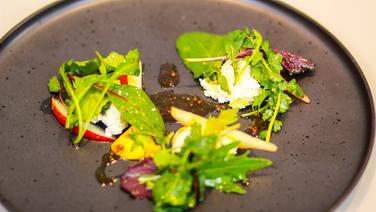 Smoked ricotta with wild herb salad and honey pears served on a rustic brown plate.  © Sascha Kirchner / solisTV 