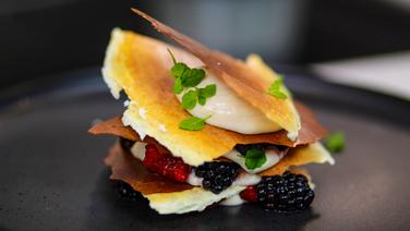 Mille Feuille von der krossen Milchhaut mit Waldmeister-Creme und frischen Beeren auf einem schwarzen Teller angerichtet. © Sascha Kirchner / solisTV 