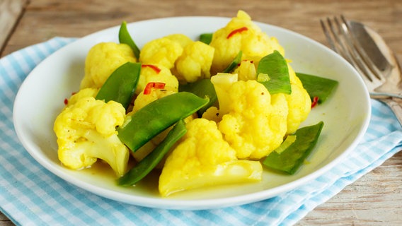 Blumenkohlcurry auf einem Teller, Besteck und Serviette auf einem Tisch. © NDR Foto: Claudia Timmann