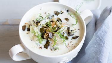 A bowl of cauliflower and fennel soup sprinkled with pumpkin seeds stands on a wooden table.  © NDR photo: Claudia Timman