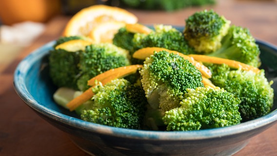 Brokkoli mit Streifen einer Orangenschale auf einem blauen Teller. © NDR Foto: Anja Deuble