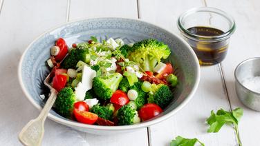 Mediterraner Brokkoli-Salat auf einemTeller. Daneben steht ein kleines Glas Öl-Balsamico-Dressing. © NDR Foto: Claudia Timmann