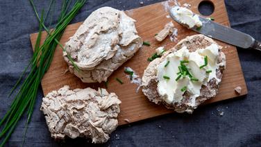 Buchweizenbrötchen mit Frischkäse bestrichen auf einem Holzbrett. © NDR Foto: Claudia Timmann