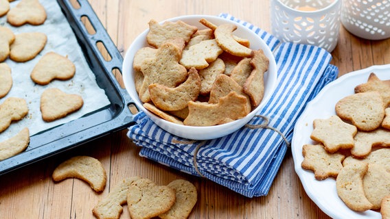 Dinkel-Plätzchen in Herz- und Sternform liegen auf einem Backblech und in Schüsseln. © NDR Foto: Claudia Timmann