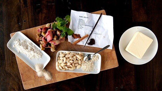 Mehl, Zucker, Mandeln, Rhabarberstücke, Butter und Gewürze auf einem Brett. © NDR Foto: Claudia Timmann