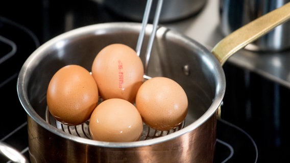 A chef lifts four eggs out of a saucepan with a slotted spoon.  © NDR Photo: Claudia Timmann