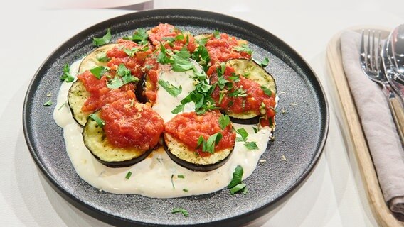 Gebackene Auberginen mit Tomaten-Sugo und Joghurt-Minz-Dip auf einem Teller angerichtet. © NDR / Fernsehmacher GmbH Foto: Gunnar Nicolaus