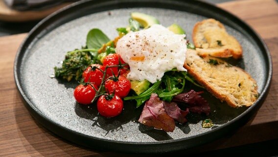 Avocadosalat mit Flusskrebsfleisch, pochiertem Ei und Baguette auf einem Teller angerichtet. © NDR / Fernsehmacher GmbH Foto: Norman Kalle