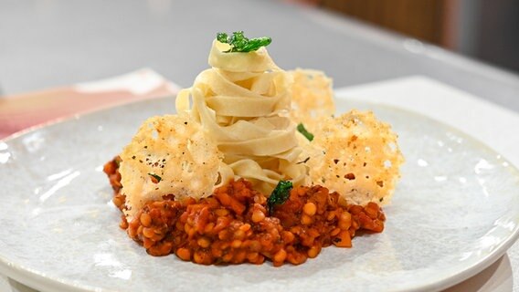 Handgemachte Bandnudeln mit Linsen-Bolognese und Parmesanchips auf einem Teller angerichtet. © NDR / Fernsehmacher GmbH Foto: Markus Hertrich