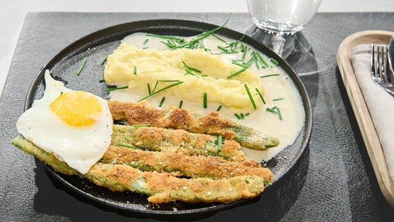 Panierte Bohnen mit Kartoffelstampf und Schnittlauchsoße auf einem Teller angerichtet. © NDR / Fernsehmacher GmbH Foto: Gunnar Nicolaus