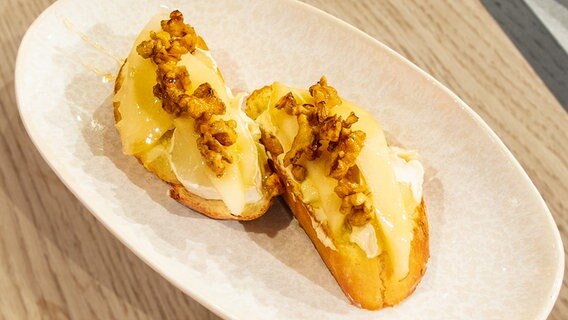 Crostini mit Ziegenfrischkäse, Birne und Walnüssen auf einem Teller angerichtet. © NDR / Die Fernsehmacher Foto: Norman Kalle