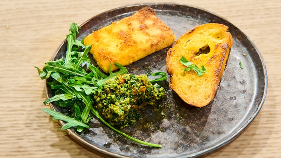 Panierter Feta mit Rucola-Pesto und Knoblauchbrot auf einem Teller angerichtet. © NDR / Die Fernsehmacher Foto: Gunnar Nicolaus