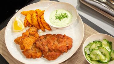 Wiener Schnitzel mit Kartoffelspalten, Gurkensalat und einer Art "grünen Soße" auf einem Teller angerichtet. © NDR / Die Fernsehmacher Foto: Norman Kalle Gunnar Nicolaus Ulrich Perrey
