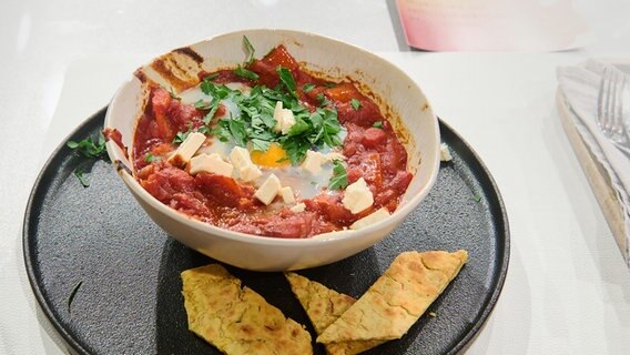 Shakshuka mit Pfannenbrot auf einem Teller angerichtet. © NDR / Fernsehmacher GmbH Foto: Gunnar Nicolaus