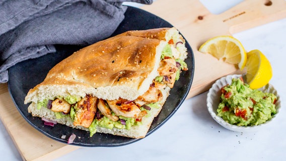 Fladenbrot mit Hähnchen auf einem Teller, daneben ein Schälchen mit Avocado-Creme und Zitronenspalten © NDR Foto: Claudia Timmann