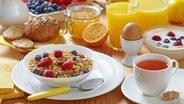 Ein reichlich gedeckter Frühstückstisch mit Müsli, Obst, Tee, Orangensaft, Ei und Brötchen. © colourbox Foto: colourbox