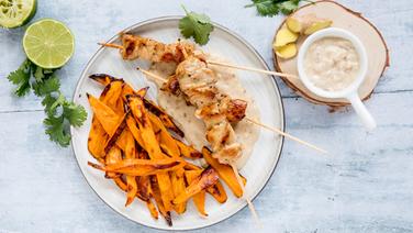 A plate of chicken skewers and sweet potato wedges and a bowl of peanut sauce are on the table.  © NDR Photo: Claudia Timmann